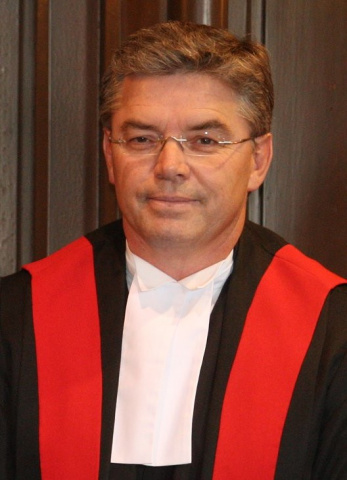 Man wearing glasses and red, black and white judicial robes.