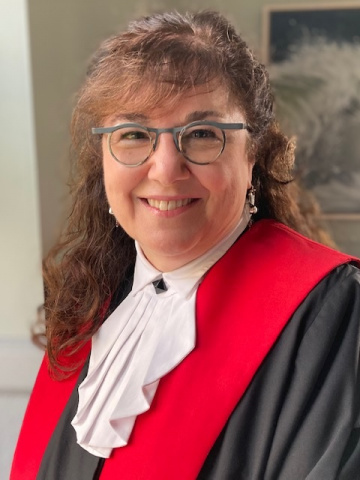 Woman with long curly brown hair and glasses in red, black and white judicial robes.