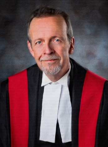 White man with a goatee wearing red, black and white judicial robes.