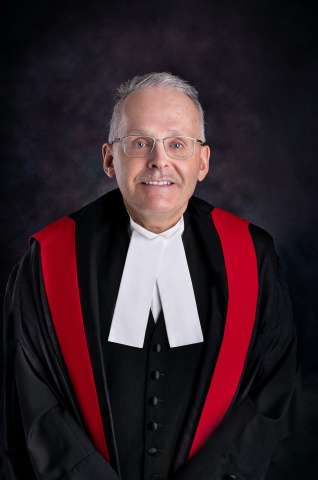 Smiling white man with glasses wearing red, black and white judicial robes.
