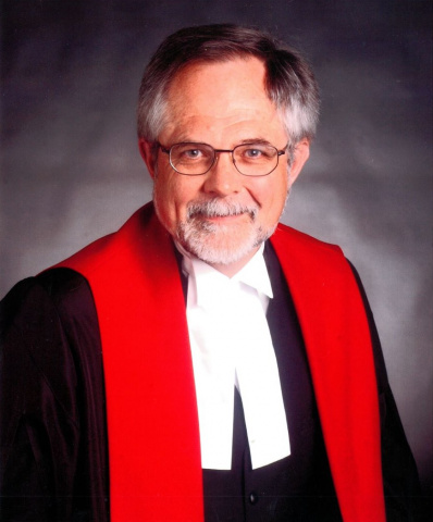 White man with glasses wearing red, white and black judicial robes.