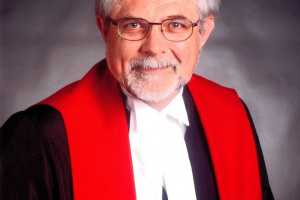 White man with glasses wearing red, white and black judicial robes.