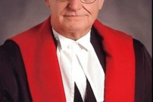 White man with white hair and glasses wearing black, red and white judicial robes.
